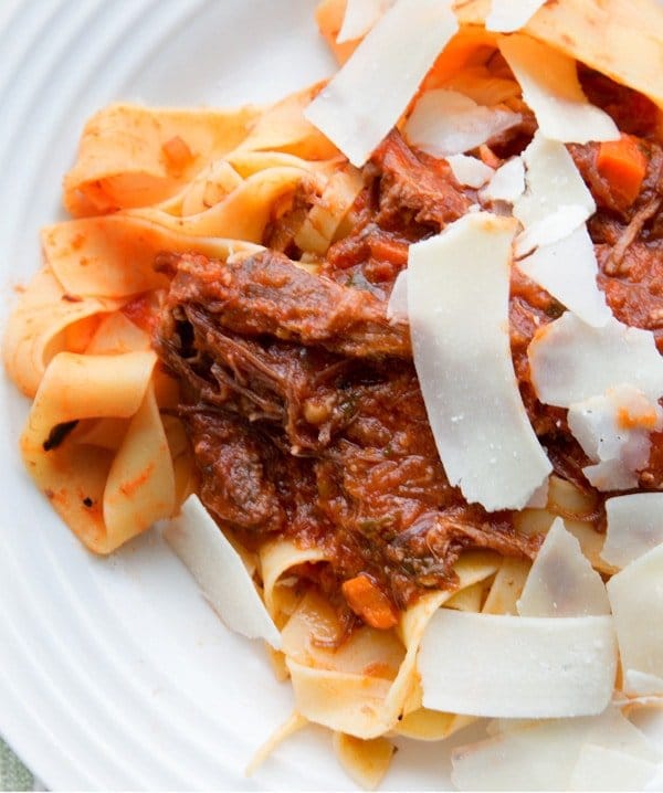 Wild Boar Ragu on Pappardelle pasta with shaved cheese slices on a white plate