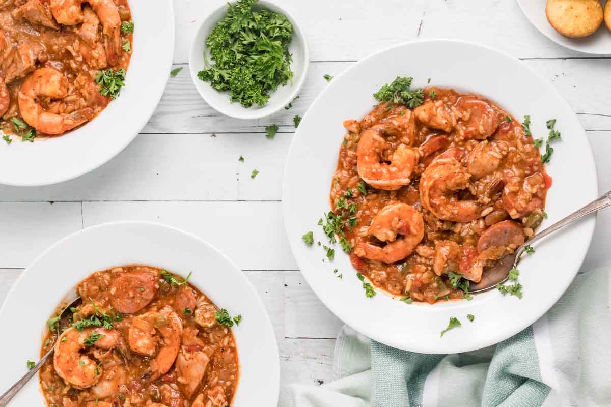 three white bowls of jambalaya with a bowl of chopped parsley 