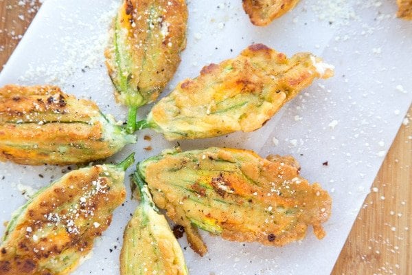 Golden Brown Fried Stuffed Zucchini Blossoms on a white paper with sprinkled romano cheese