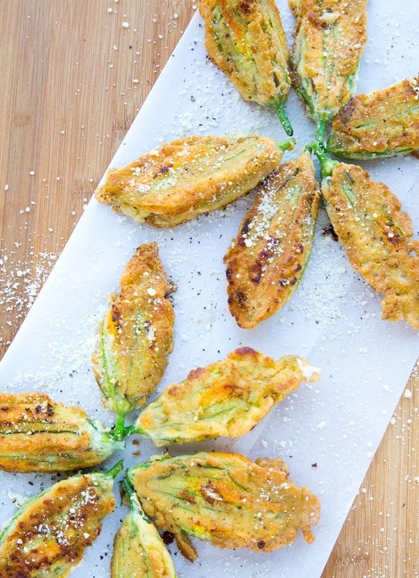 Golden Brown Fried Stuffed Zucchini Blossoms on a white paper with sprinkled romano cheese