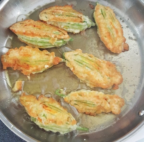 Golden Brown egg battered stuffed blossoms in a saute pan with hot oil