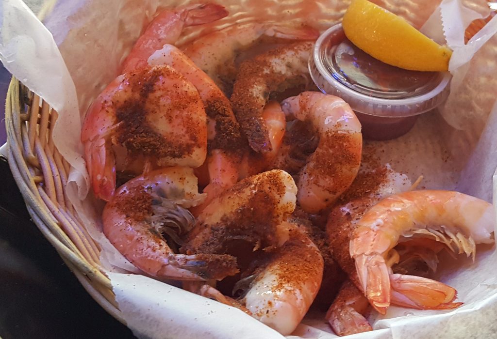 old bay seasoned steamed shrimp in a basket with cocktail sauce and a lemon wedge