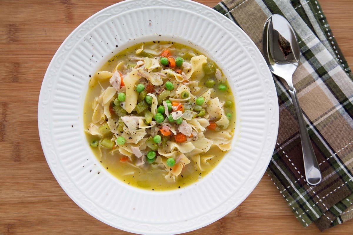 overhead view of turkey noodle soup in a white bowl.