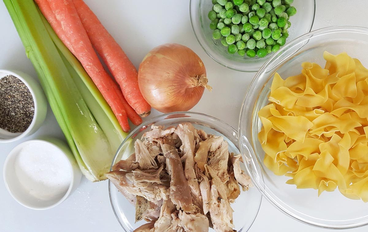 ingredients to make turkey noodle soup on a white cutting board