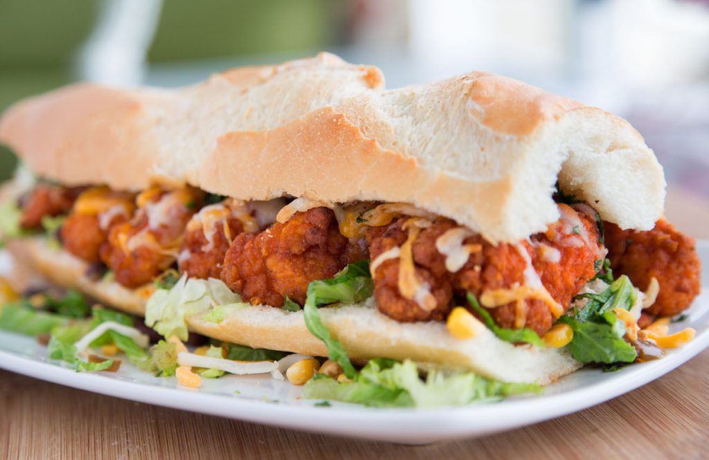 side view of a buffalo chicken po boy on a long roll on a white plate