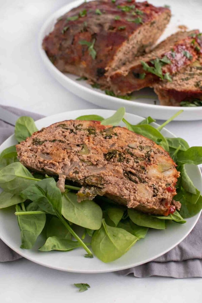 slice of meatloaf on baby spinach with the rest of the meatloaf in the background