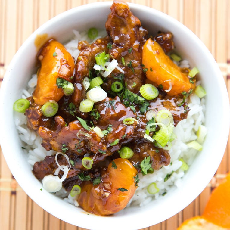 overhead view of asian style tangerine beef over rice in a white bowl garnished with scallions and parsley