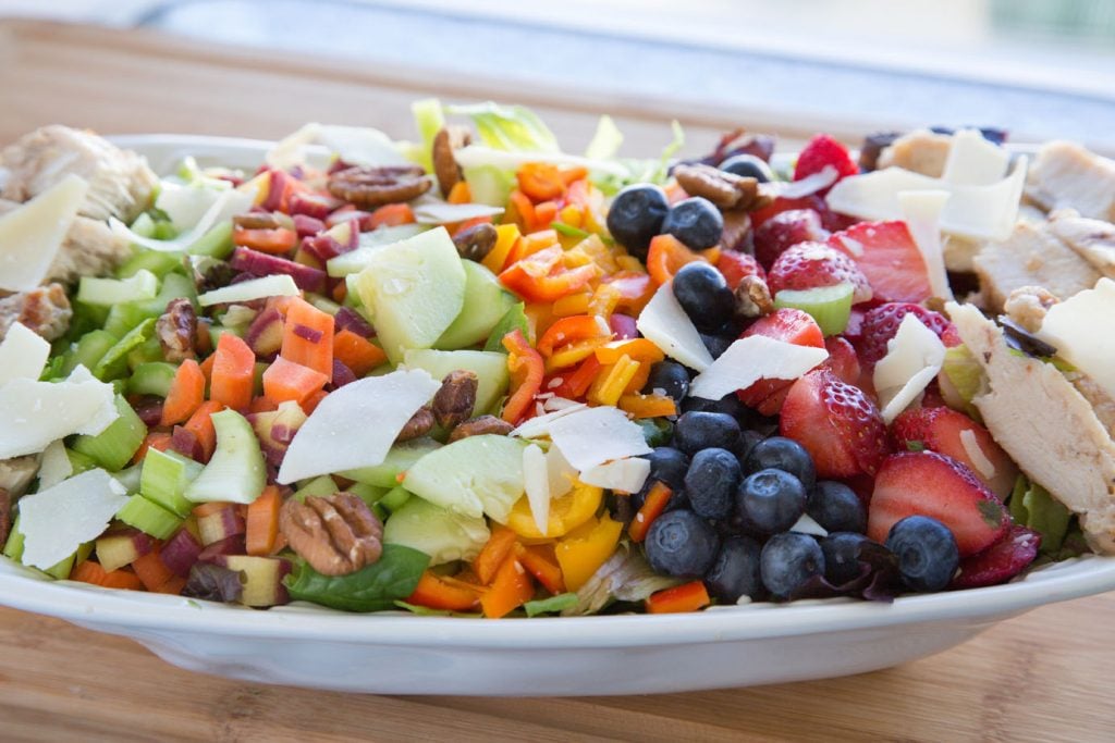 dinner salad with a variety of vegetables, berries , chicken, nuts and cheese on a bed of greens on a large white platter