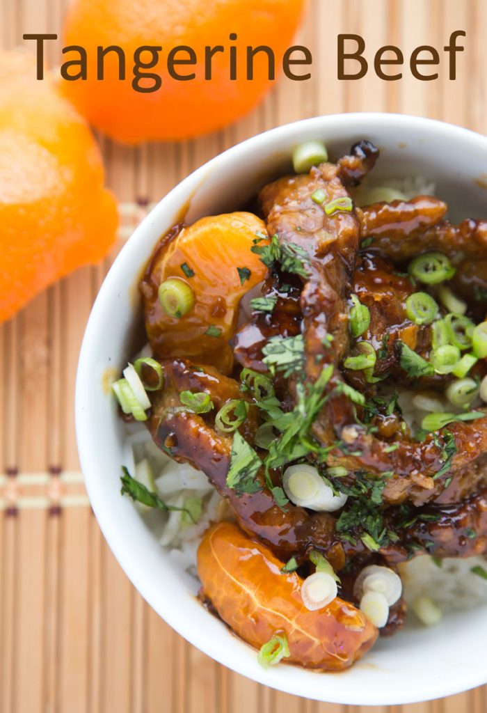overhead view of asian style tangerine beef over rice in a white bowl garnished with scallions and parsley with tangerines next to the bowl