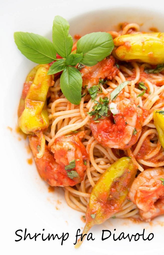 overhead view of shrimp fra diavolo over linguine ina white bowl with a sprig of basil in the corner