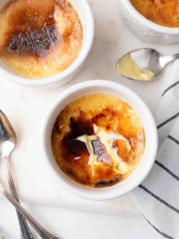 overhead view of 3 cups of creme brulee with one of the sugar tops cracked showing the custard