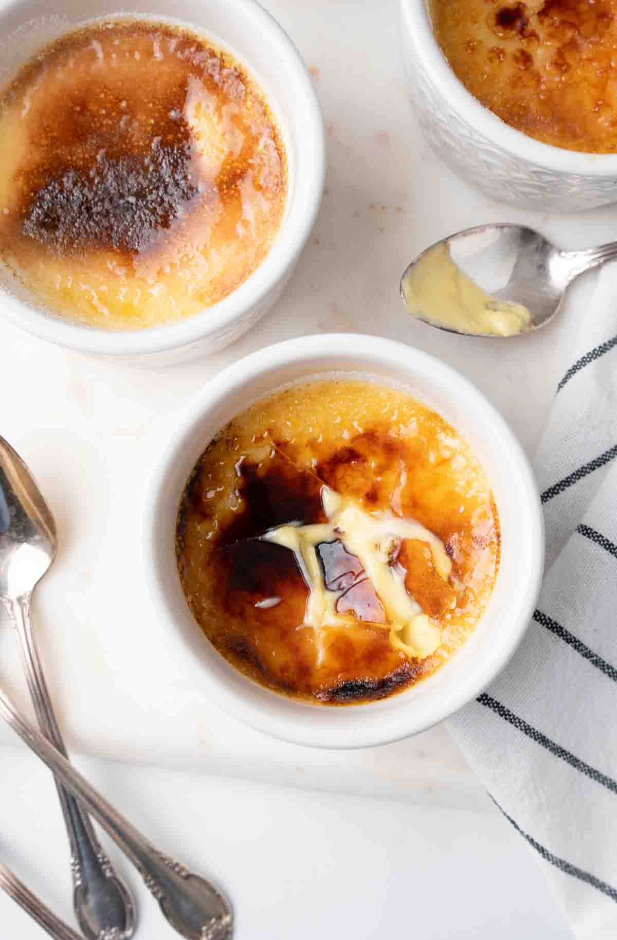 overhead view of 3 cups of creme brulee with one of the sugar tops cracked showing the custard