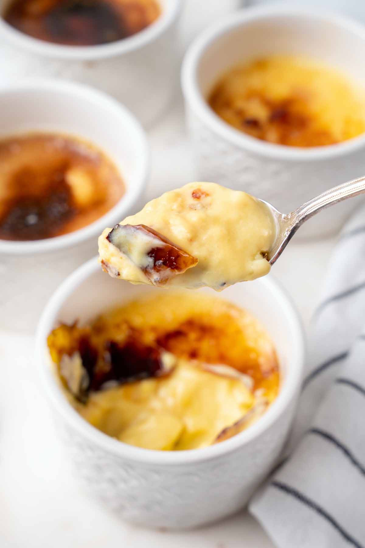 white cups of creme brulee with a spoonful of custard above one of them