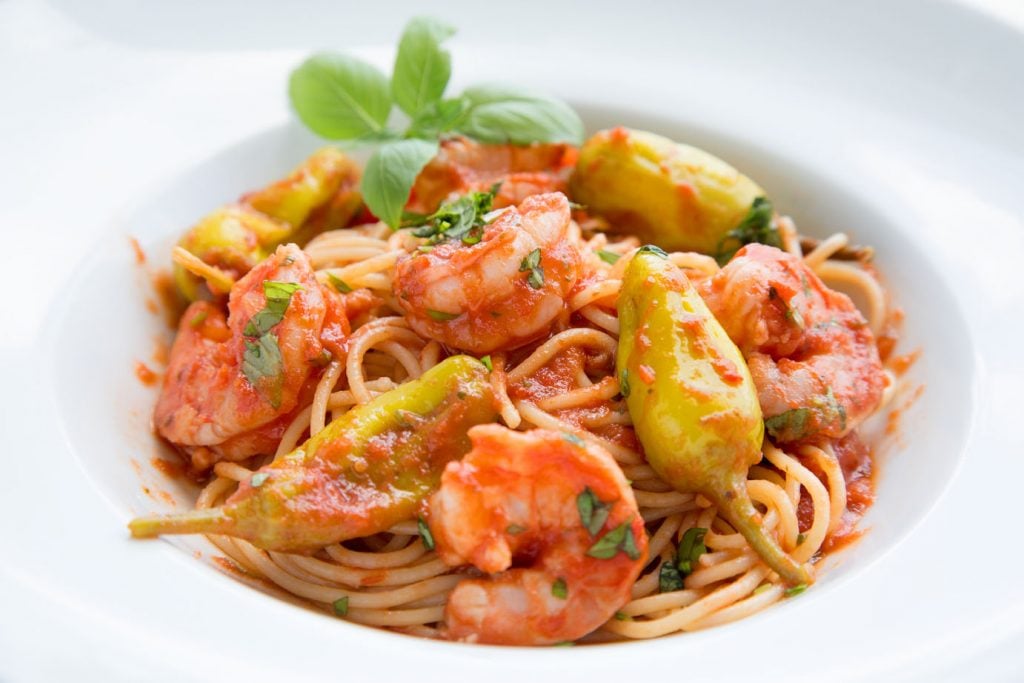 shrimp fra diavolo over linguine ina white bowl with a sprig of basil in the corner