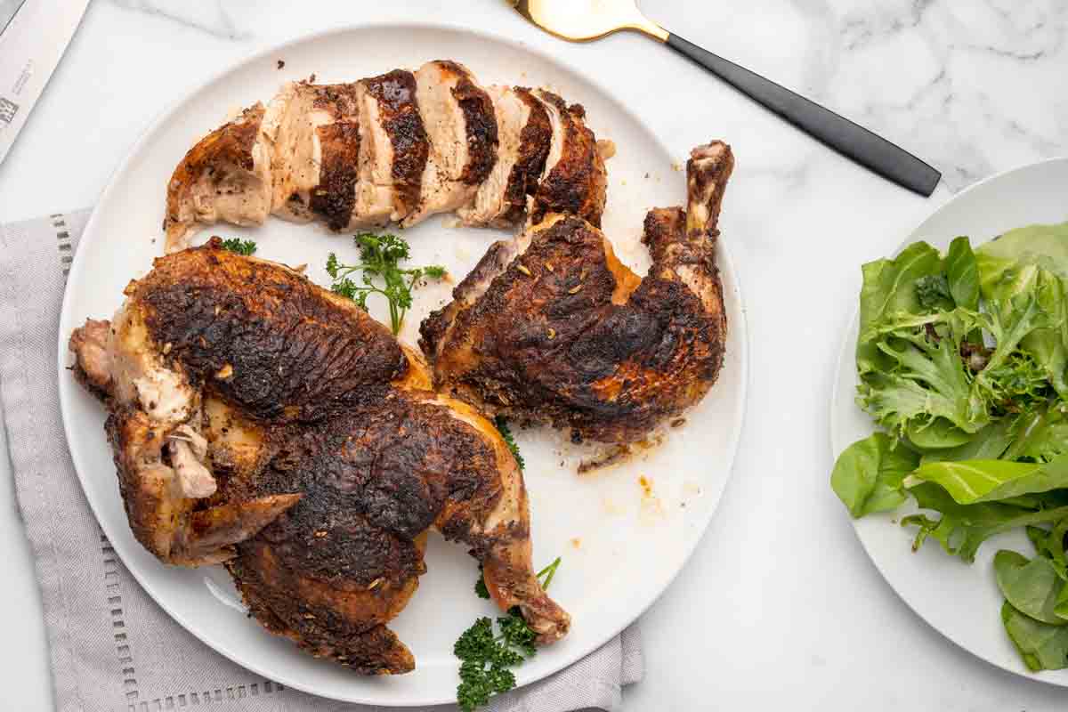 blackened half chickens on white plate, one of them sliced