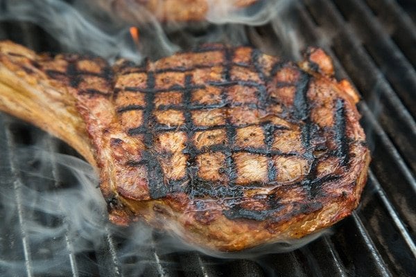 Ribeye on grill cooking with crosshatch marks and smoke is coming off the steak
