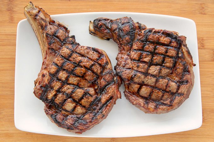 2 grilled ribeye steaks showing crosshatch marks from the grill on a white oblong platter