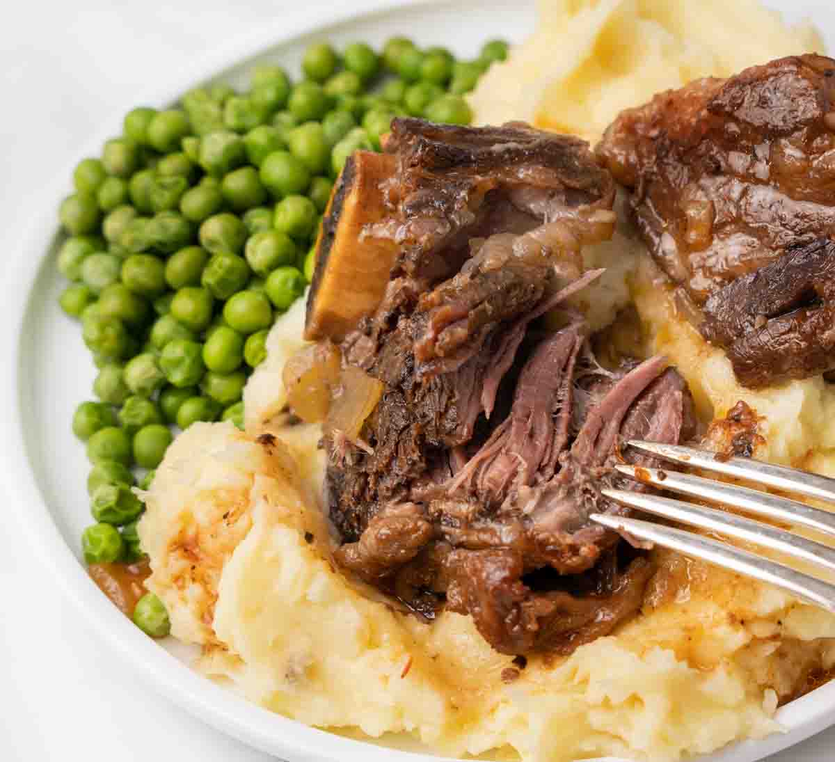 fork taking piece of fall apart meat from short rib on a bed of mashed potatoes
