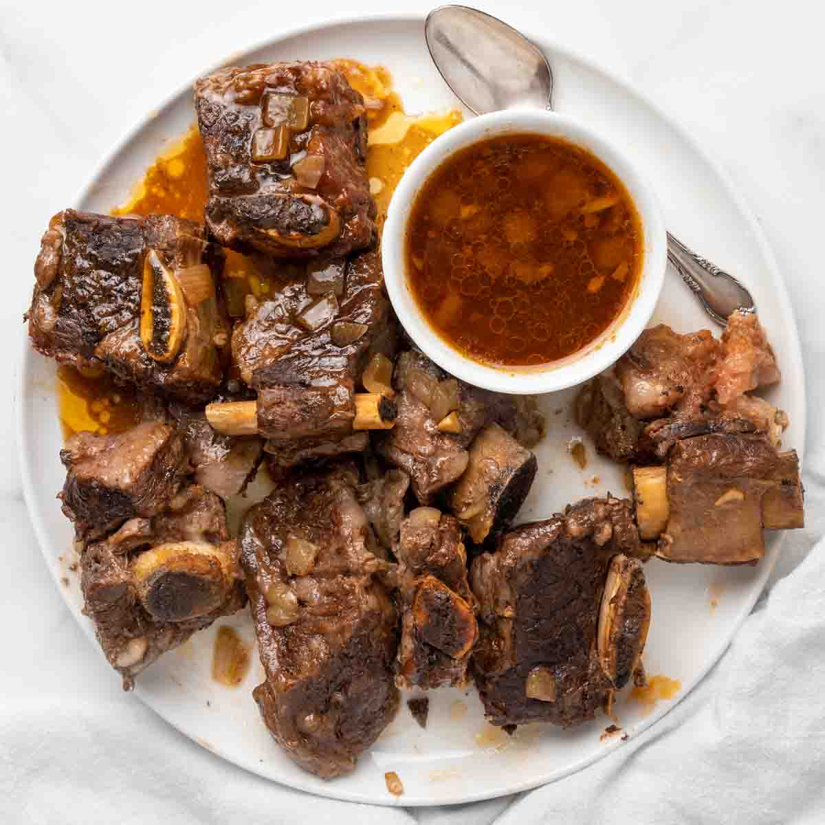 beef ribs on a white plate with sauce in a ramekin