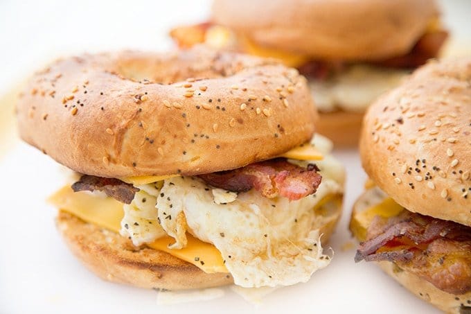 close up view of a everything bagel breakfast sandwich with one blurred in the background