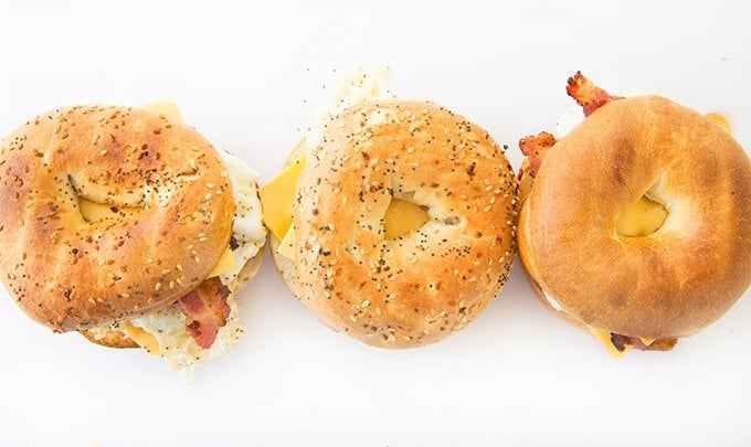 overhead view of two everything bagel sandwiches and one plain bagel sandwich