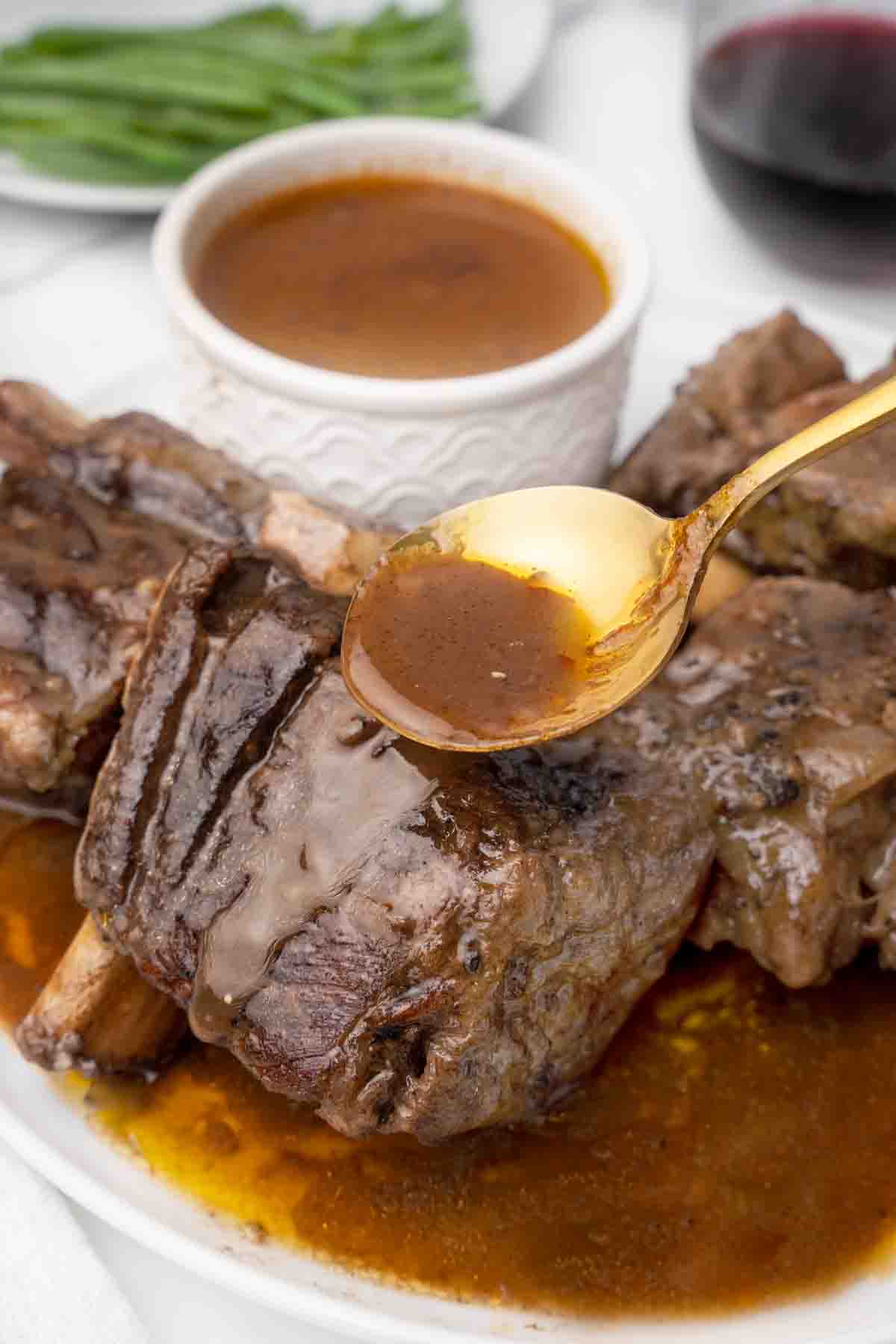 spoon with sauce being poured on short ribs on a white platter