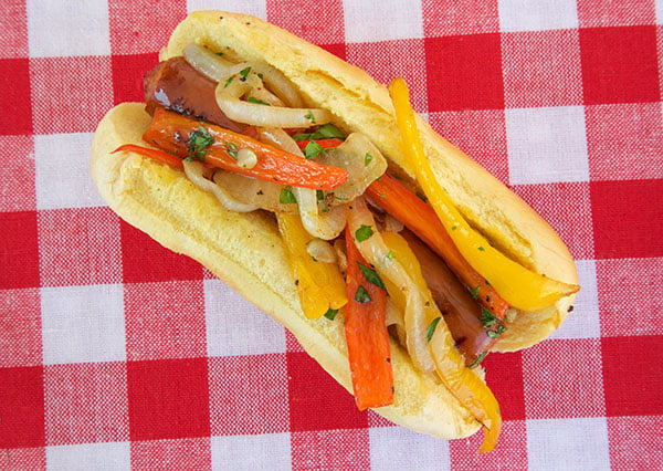 cheddar wurst on a hot dog bun topped with sauteed peppers and onions