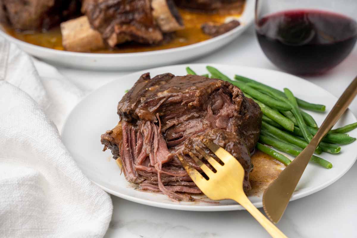 fork pulling meat off a short rib on a white plate