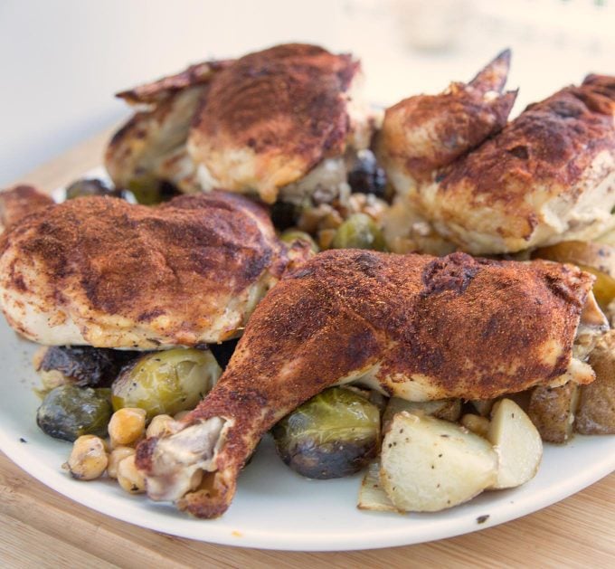 side view of Smoky Roasted Chicken quarters with Brussels Sprouts and Chic Peas on a white platter