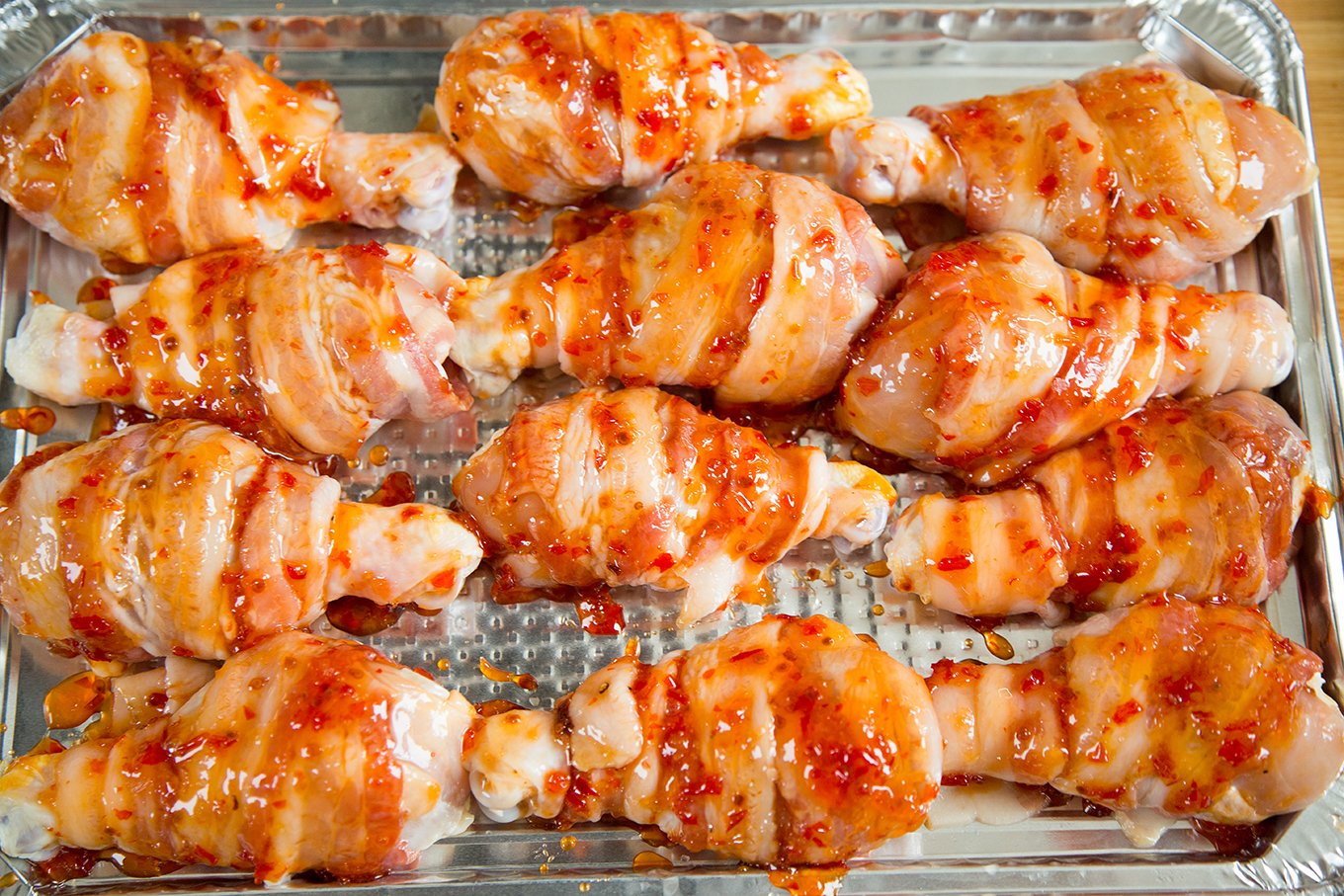 Bacon wrapped chicken legs with a sweet chili glaze on a foil baking sheet