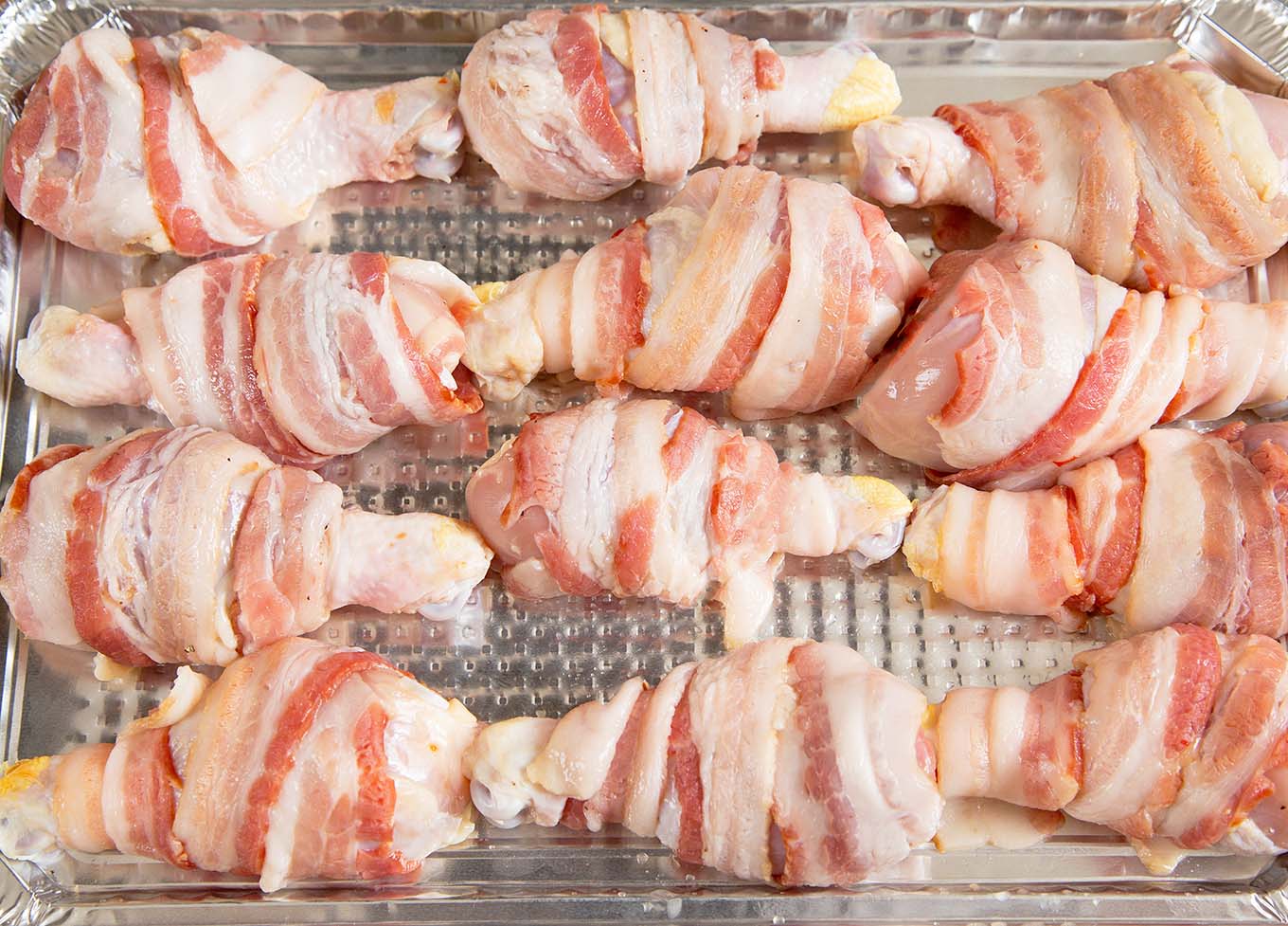 bacon wrapped chicken legs on a foil tray