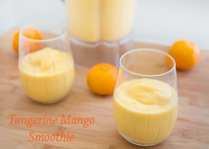 2 glasses of Tangerine Mango Smoothie with tangerines and a blender in the background