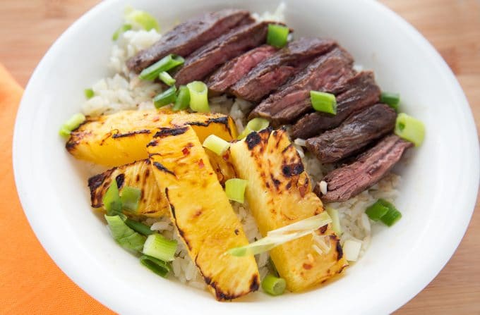 overhead shot of grilled pineapple and grilled flank steak over rice in a white bowl