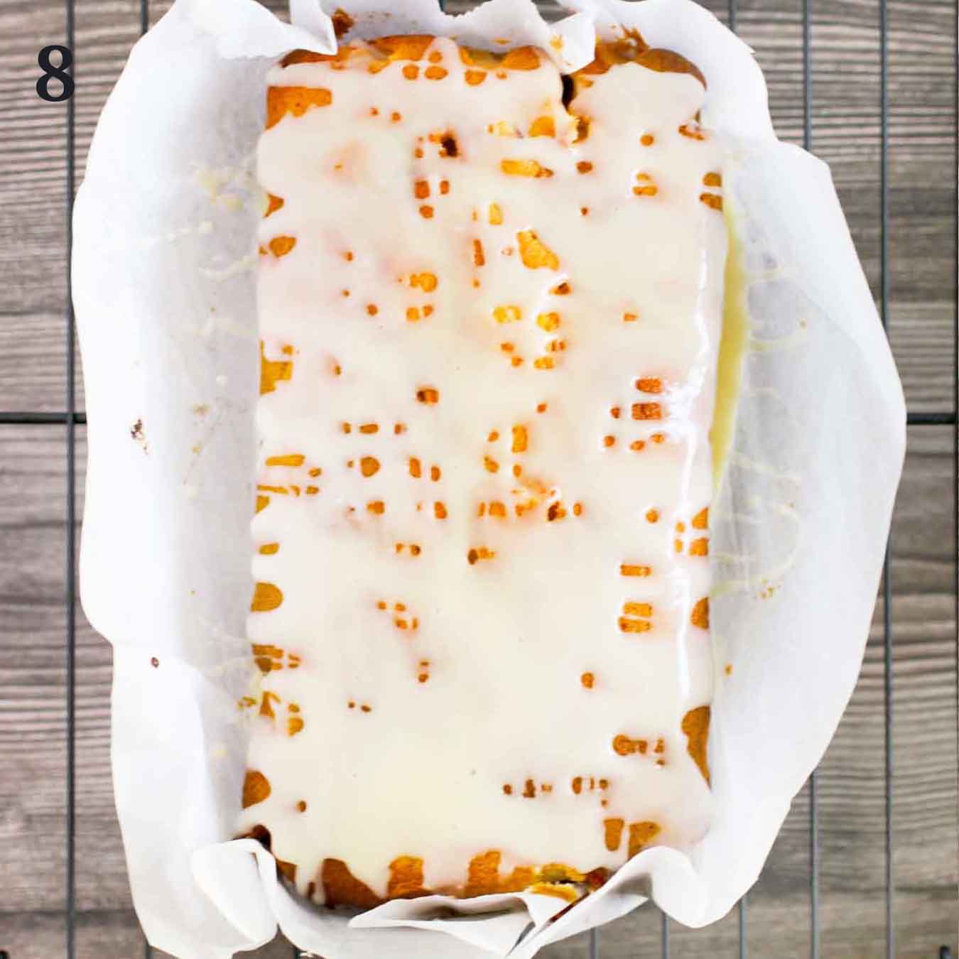 Cranberry orange bread with sweet orange glaze on parchment paper on a wire rack.