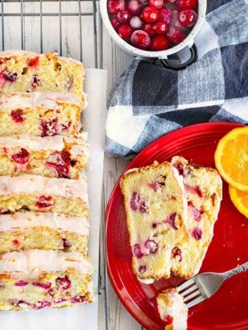 Slices of cranberry orange loaf on a wire rack next to slices on a red plate.