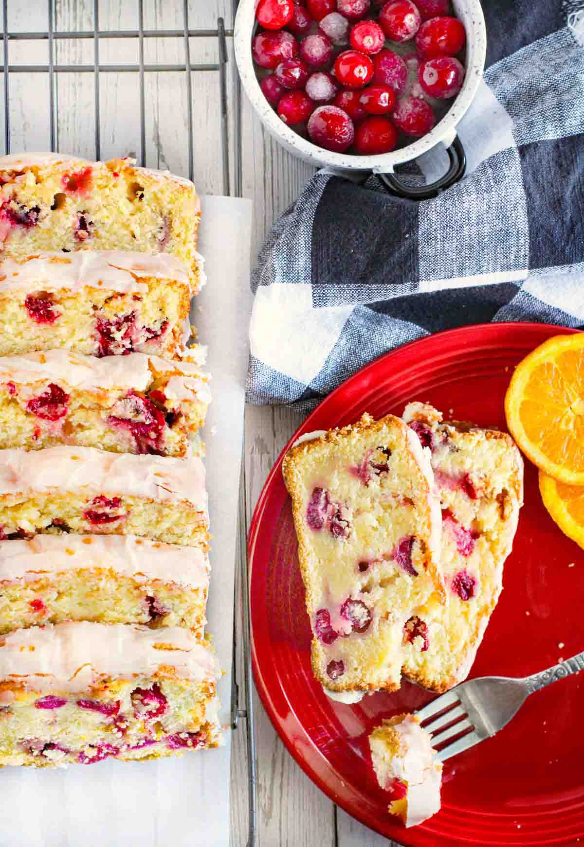 Slices of cranberry orange bread on a wire rack next to slices on a red plate.