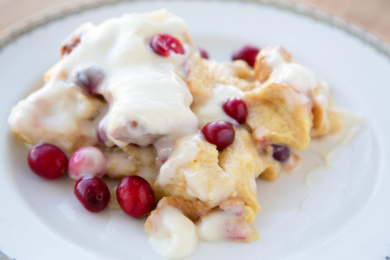 Cranberry Eggnog Bread Pudding with a Bourbon Cream Cheese Frosting on a white plate