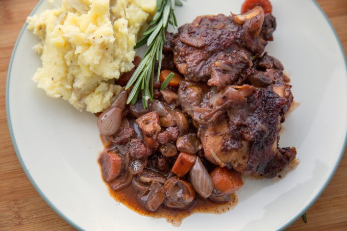Coq au Vin and mashed potatoes on a white plate with a sprig of rosemary