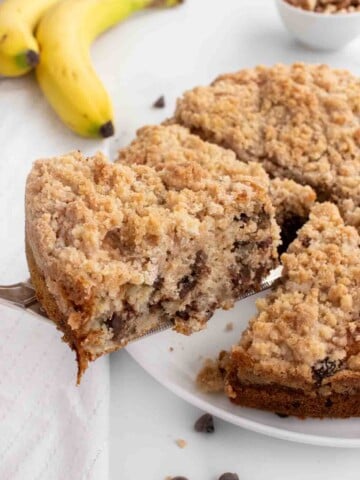 slice of banana crumb cake being taken out of whole cake