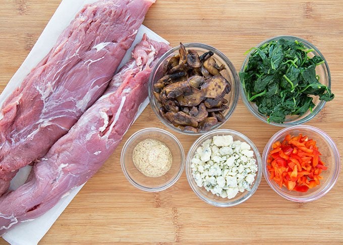 pork tenderloin and ingredients for stuffing in bowls sitting on a cutting board