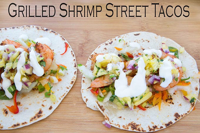 two grilled shrimp street tacos sitting on a cutting board