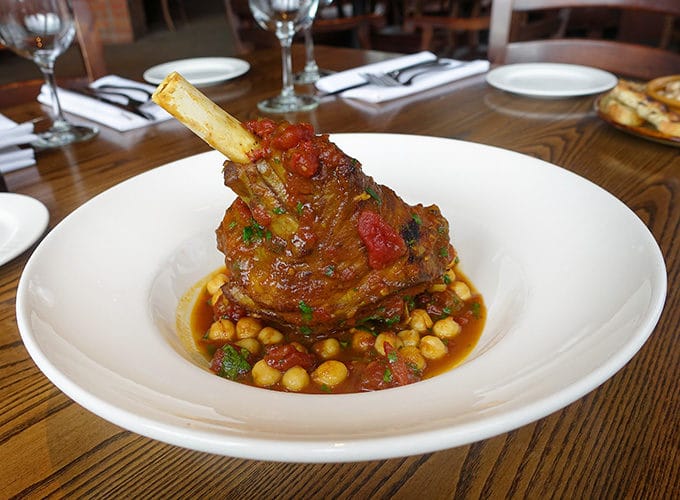 Braised Lamb Shank with tomato Chick Pea Ragout served in a white bowl on a table 