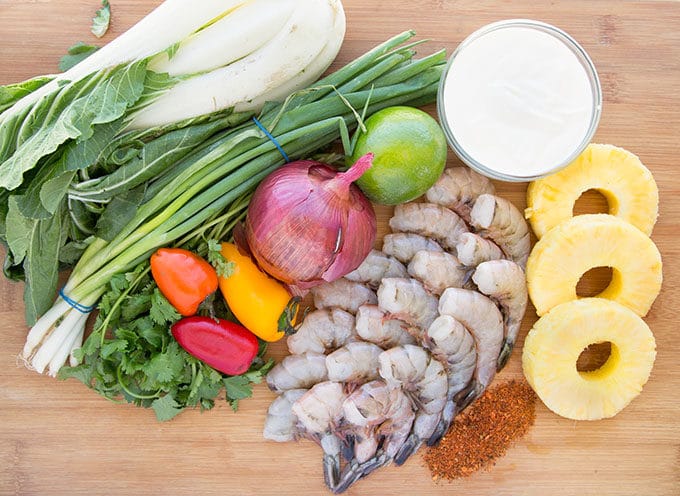 shrimp, pineapple, peppers, onion, lime, cilantro, green onions and bok choy on a cutting board