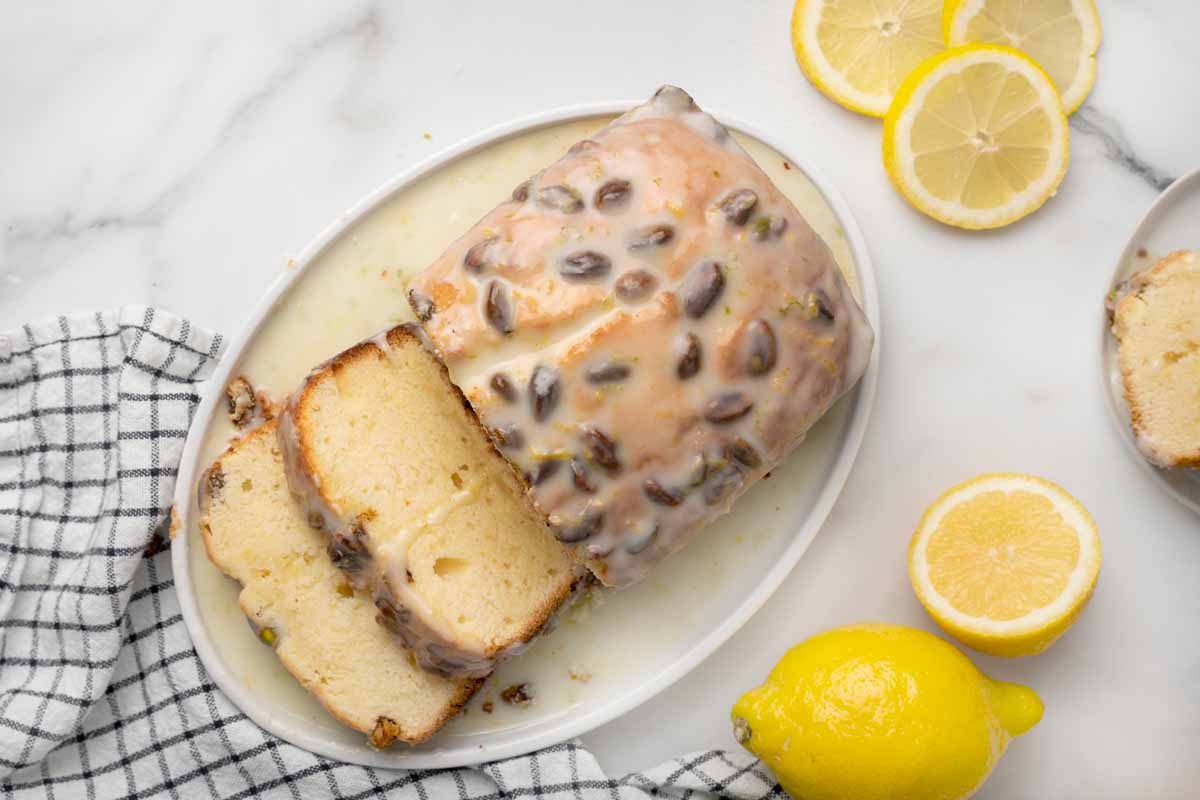 overhead view of sliced lemon pound cake on a white plate with lemons next to it