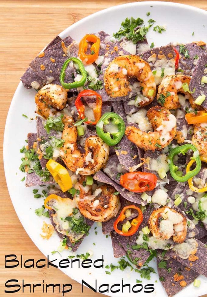 blackened shrimp nachos with melted cheese and peppers on a white plate sitting on a cutting board