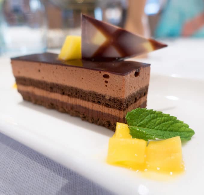 chocolate mousse cake on a white plate with mango chunks and a mint leaf