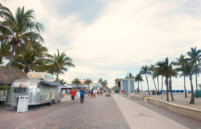 boardwalk with airstream food truck on one side with palm trees and beach on the other side