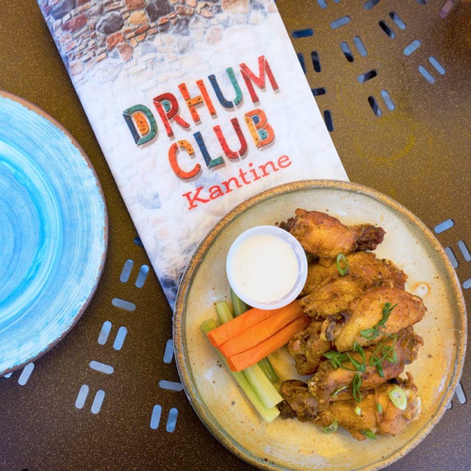 jerk seasoned chicken wings on a tan plate with carrot and celery sticks and ranch dressing. Menu under the plate, with part of a blue plate in the picture