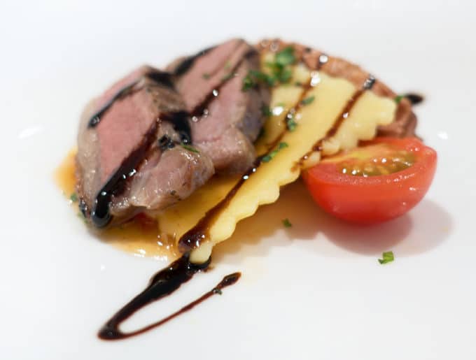 slices of roasted lamb served with ravioli and tomato on a white plate