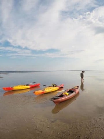 Kayaks on the mud flats of Caraquet, with one person looking out into the distance.